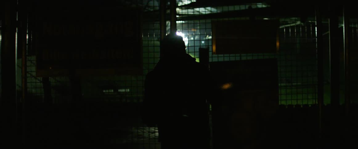 Man walks towards a metal fence in the dark