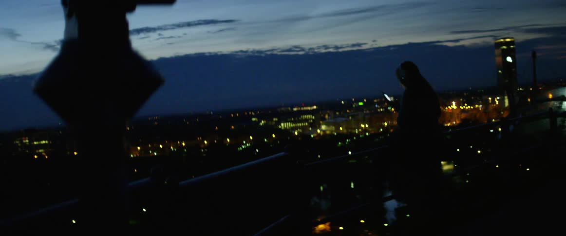 A girl stands with the city skyline in front of her as she uses her cell phone