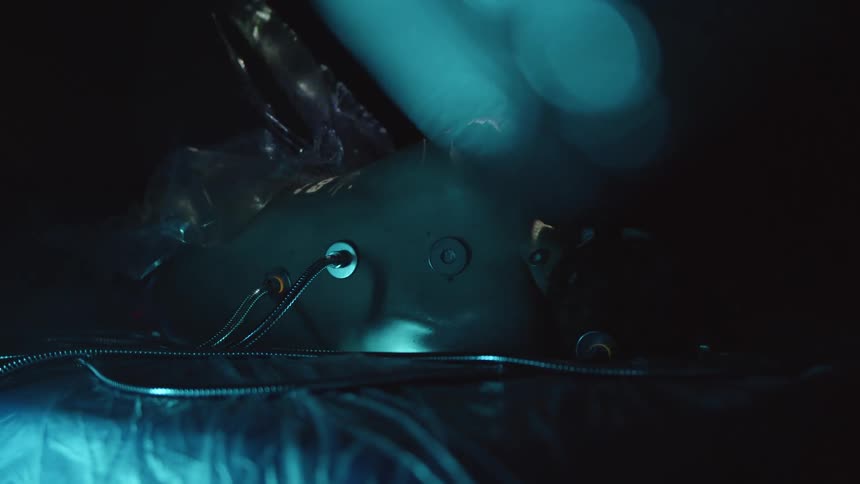 Plastic wrap is pulled off of a human body with lighted cables running into its back