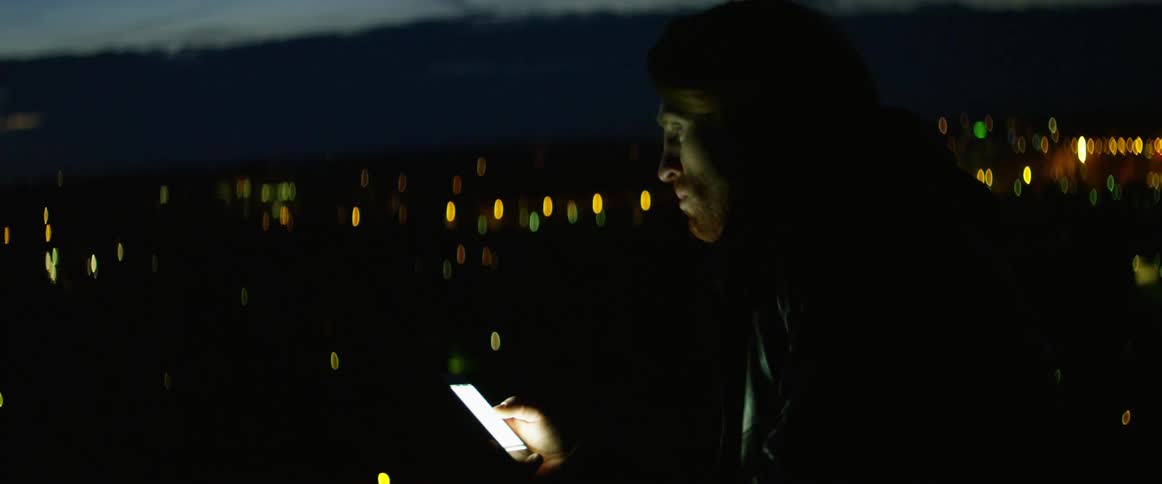 A man uses a smartphone outside in the dark