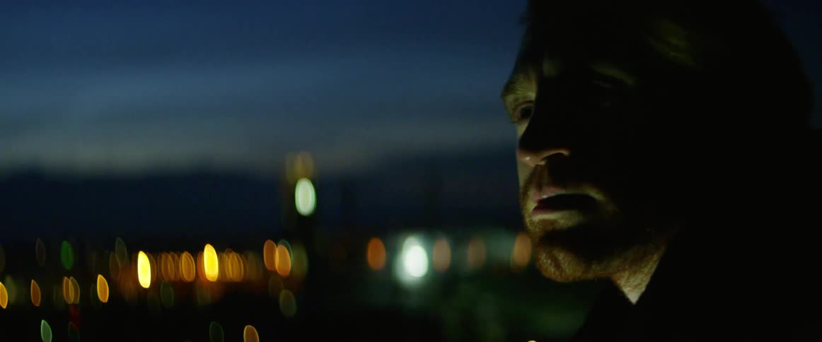 Bearded man stands close to city lights at sunset
