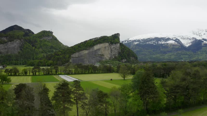 Green farm land stretches in front of a mountain range