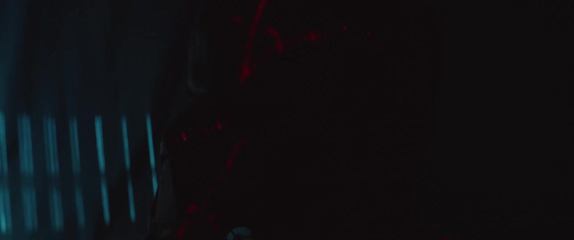 A man with his face partially covered stands in the dark