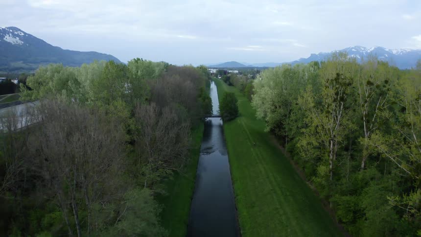A canal with a bridge and trees with mountains in the background