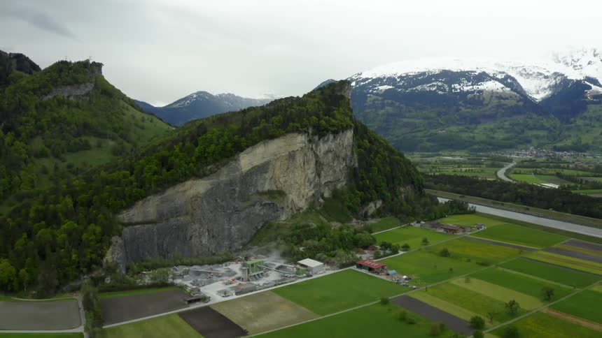 Farmland and buildings sit near a sheer mountain cliff