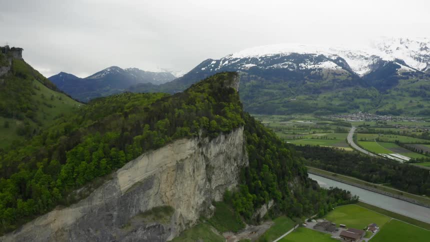 A large cliff and a snow covered mountain surrounded by greenery
