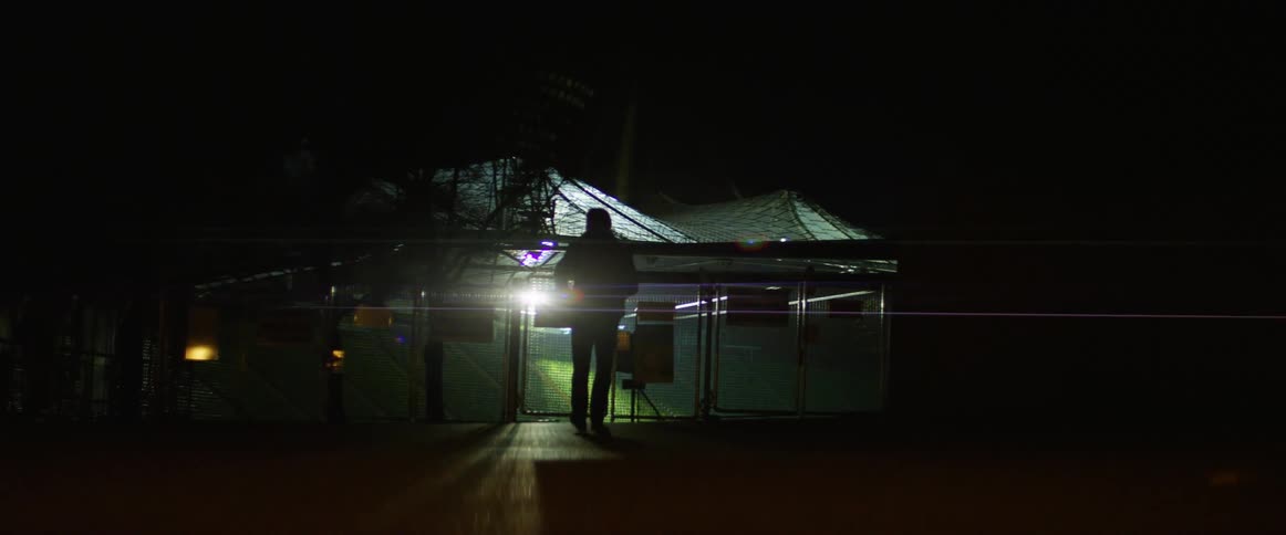 A man walks toward a restricted shelter outdoors thats blocked with a chain link fence
