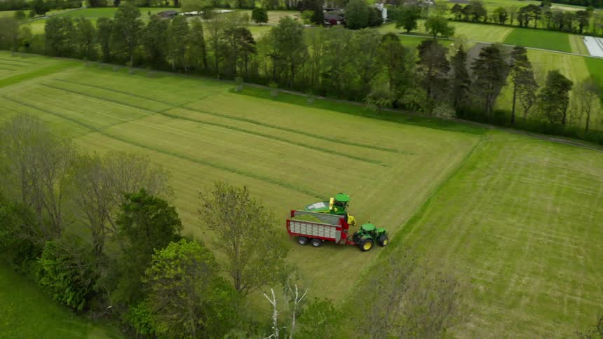A harvester traveling along a field dumping its harvest into the trailer of a tractor traveling next to it