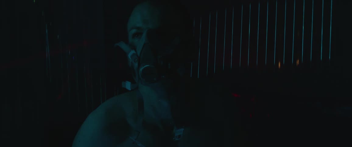A white man sits in a room wearing a face mask