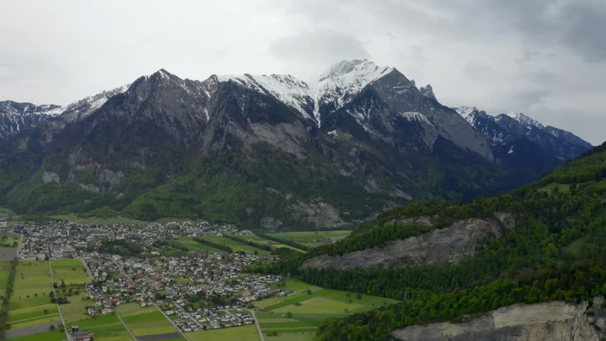 A town and green fields in the valley of a mountain range