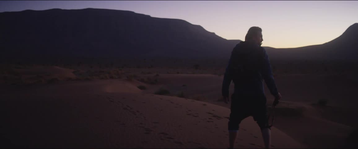 Man walks on the sand dune in the desert at dusk