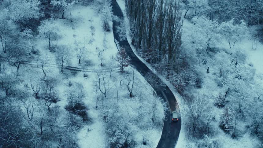 A vehicle traveling along a winding road through a snowy woodland