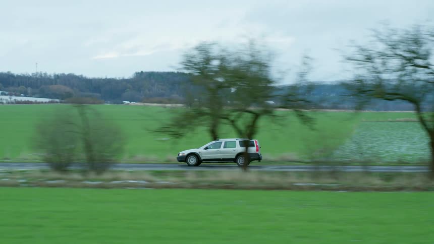 A vehicle drives down a narrow road outside a small town in a rural area