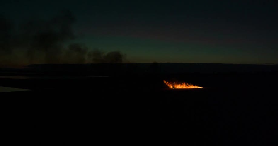 Wildfire burns producing cloud of black smoke visible against horizon at night