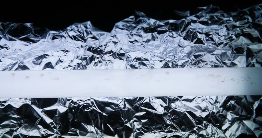 Glowing bar hovers over crinkled aluminum foil creating shadows and highlights