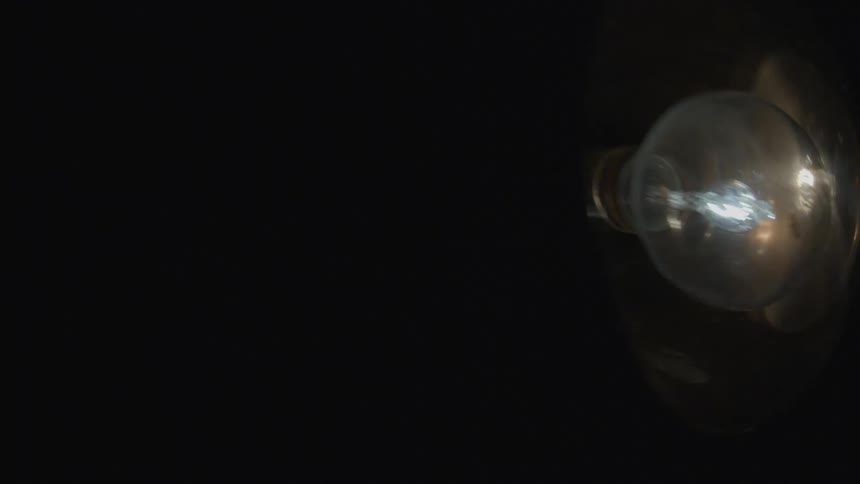 A light bulb set in a metal shade swings back and forth
