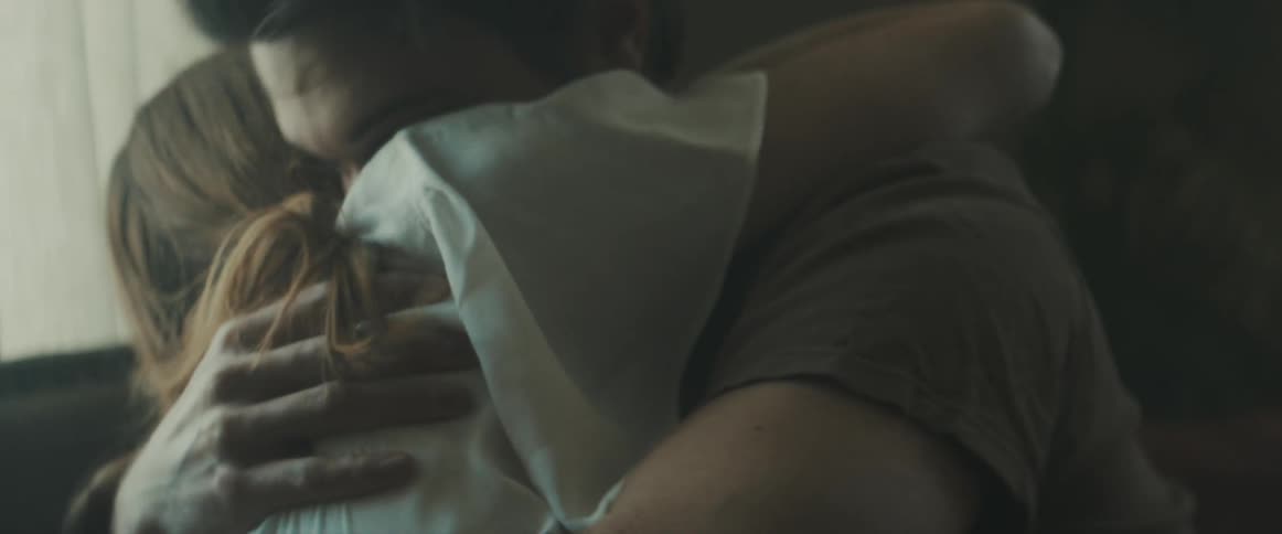 A young woman and her boyfriend hug and then kiss on the couch