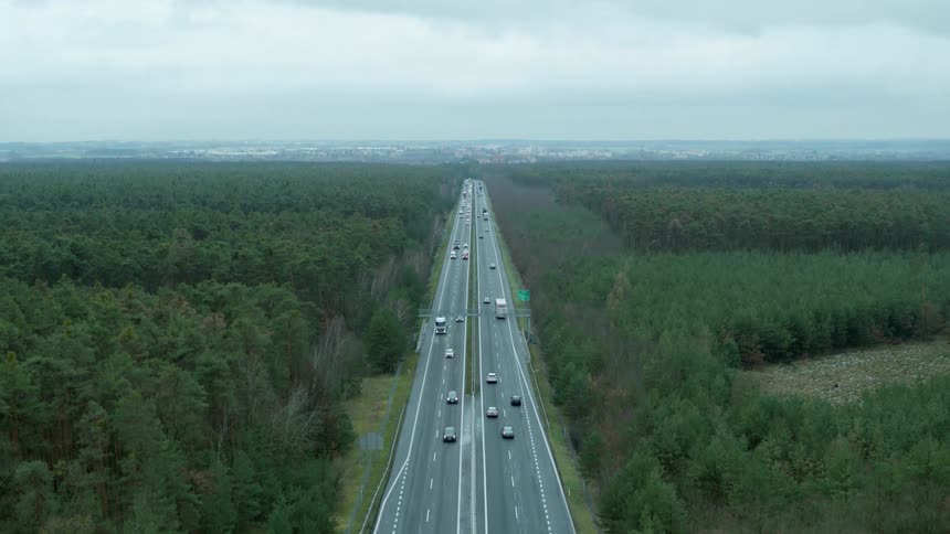 Traffic traveling along a busy freeway through a vast woodland towards and away from a city in the distance