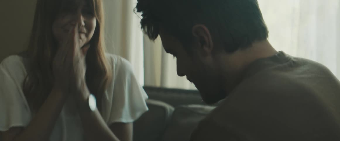 A couple sit on a couch and hug amid smiles