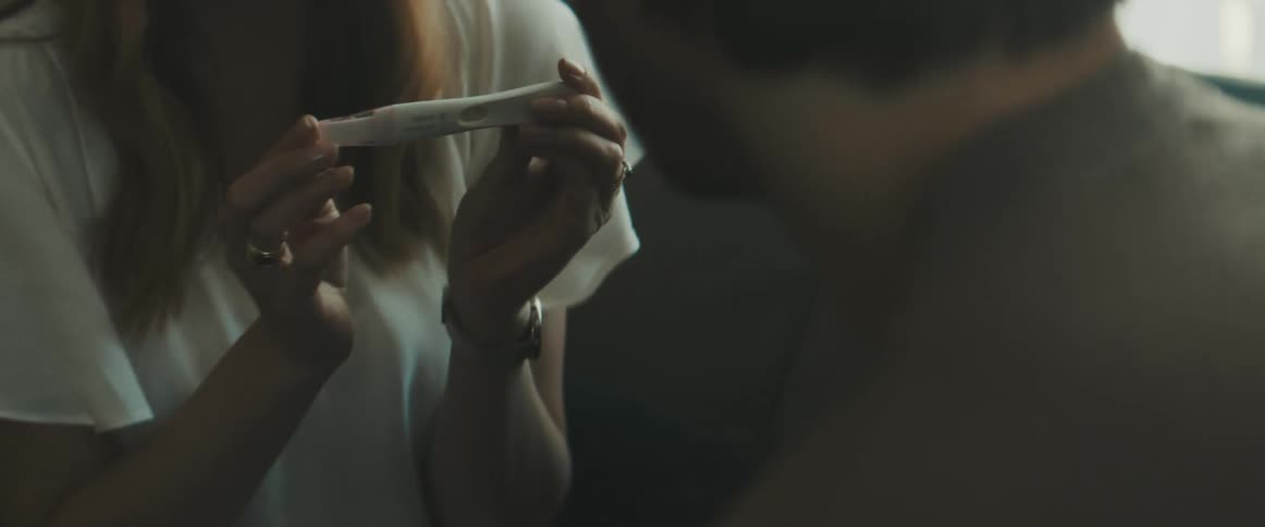 A smiling woman showing a man the results of a pregnancy test before the two embrace