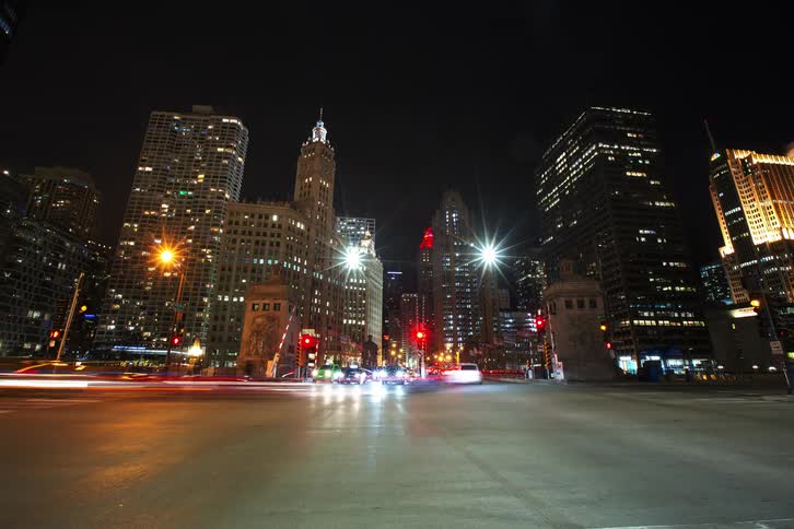 Cars travel on a busy city street near skyscrapers at night