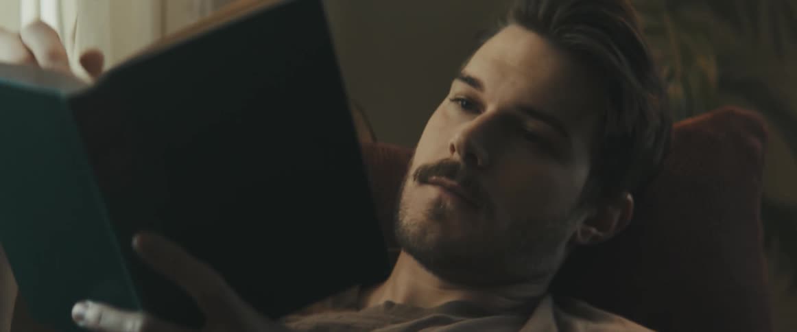 Man lying down on the sofa reads a book