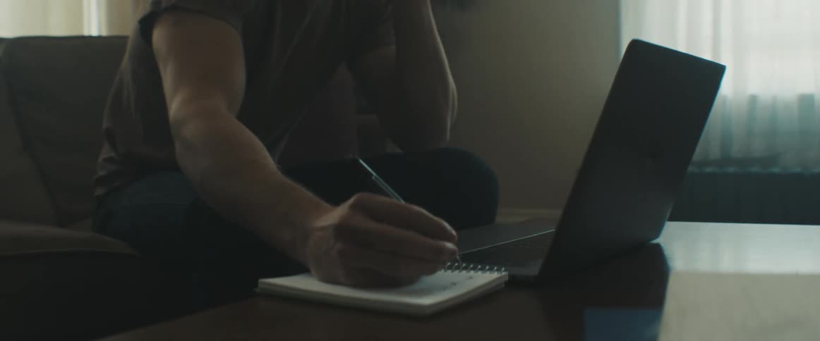 Man sitting on the sofa speaks on the phone and takes notes