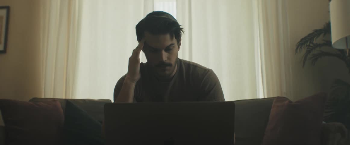 A man sits on his couch and looks at his laptop