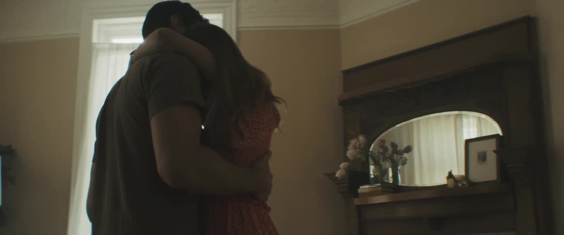 A man and woman dancing slowly in the living room of a house illuminated by sunlight