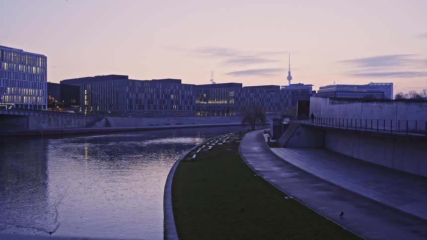Person walks along bridge paralleling waterway near low rise buildings