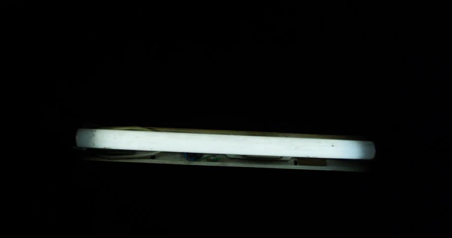 A flickering fluorescent light repeatedly brightening and dimming as it tilts up and down in the darkness