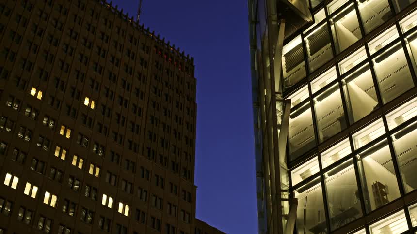 Two buildings in a downtown area lit up with interior lights