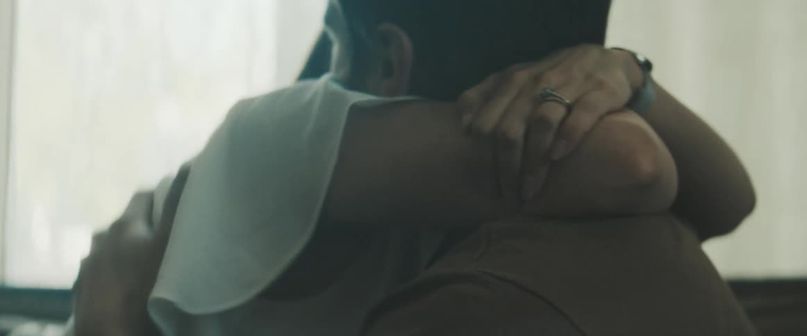A man and a woman embrace while sitting on a couch in a living room