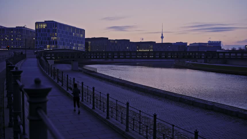 A person runs next to the water as other pedestrians walk across the bridge