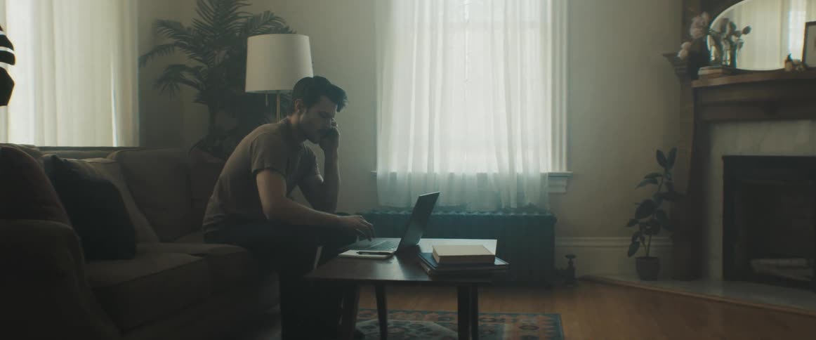 Man sitting on the sofa speaks on the phone and uses his laptop