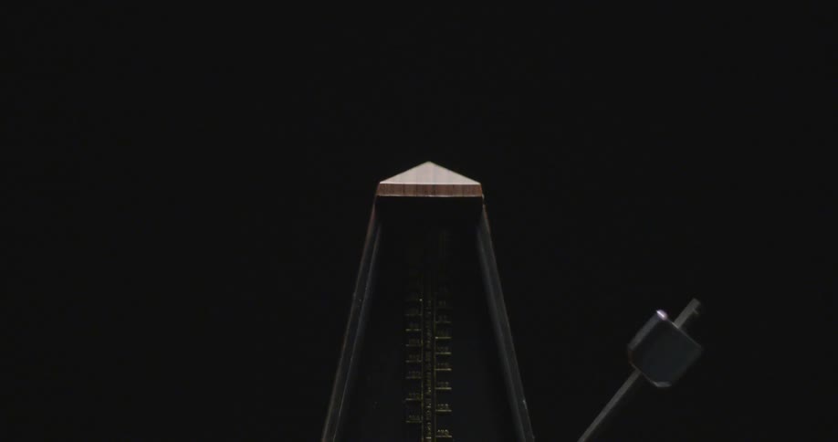 A metronome swings back and forth in the dark