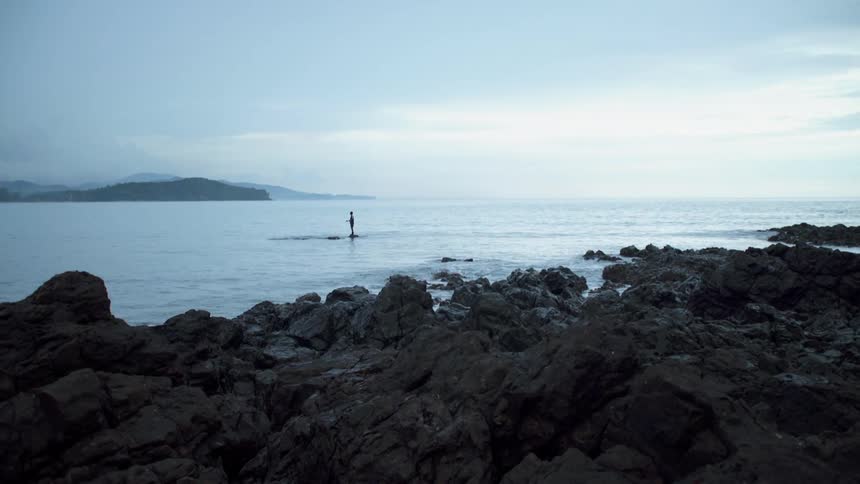 A person stands on a rock in a bay and fishes