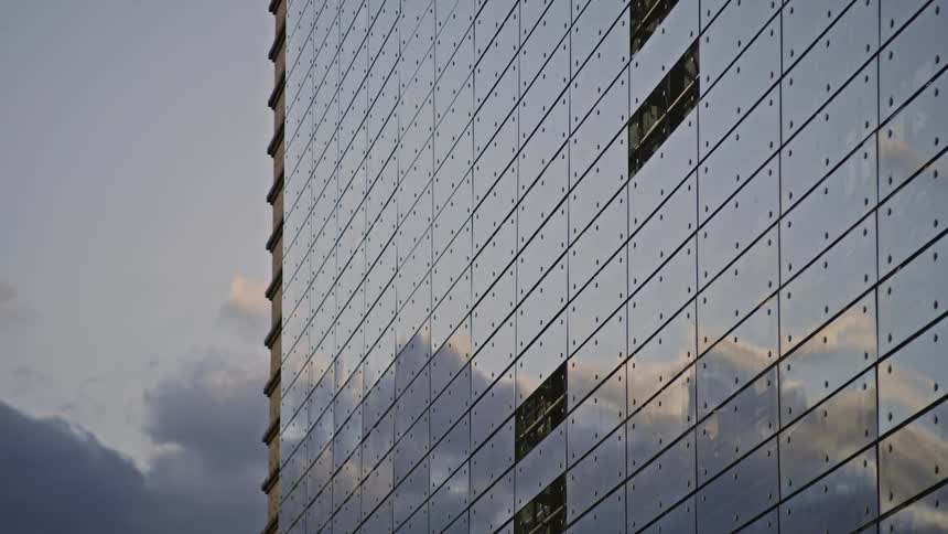 A large buildings windows reflect clouds moving across the sky