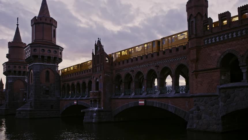 A train traffic and pedestrians travelling across a large elaborately crafted stone bridge spanning a river