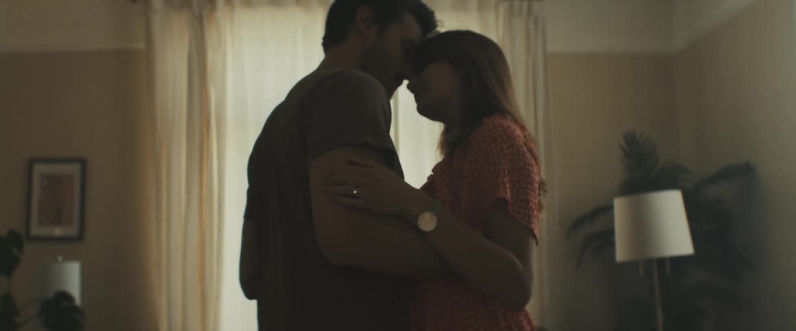 Man and woman kissing and dancing slowly in the dimly lit living room of a house