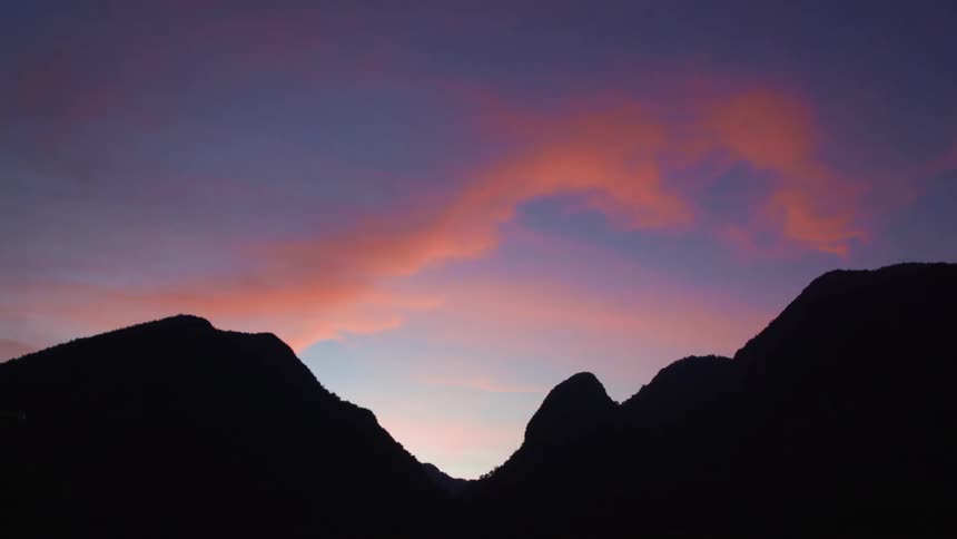 Clouds lit up by the sun float over a dark mountain range