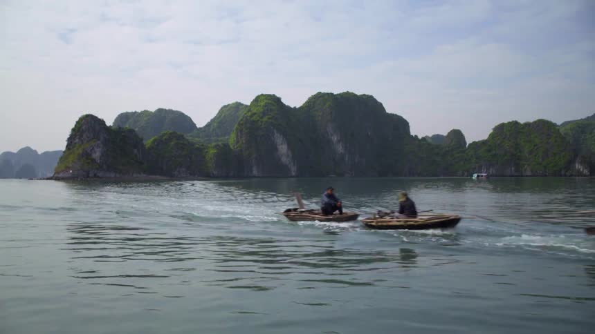 People sit on two row boats that are being pulled by a power boat across the water