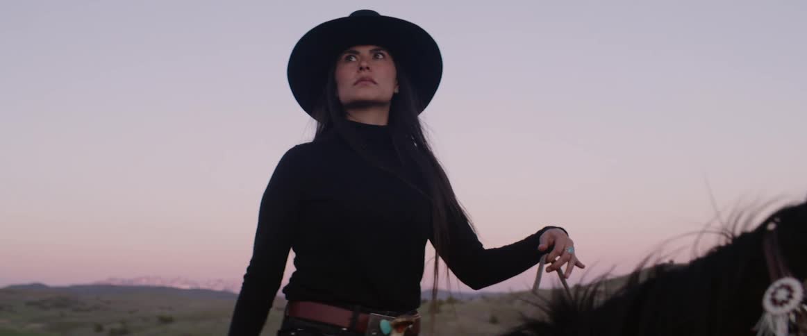Woman wearing a wide hat rides a dark horse and looks around anxiously