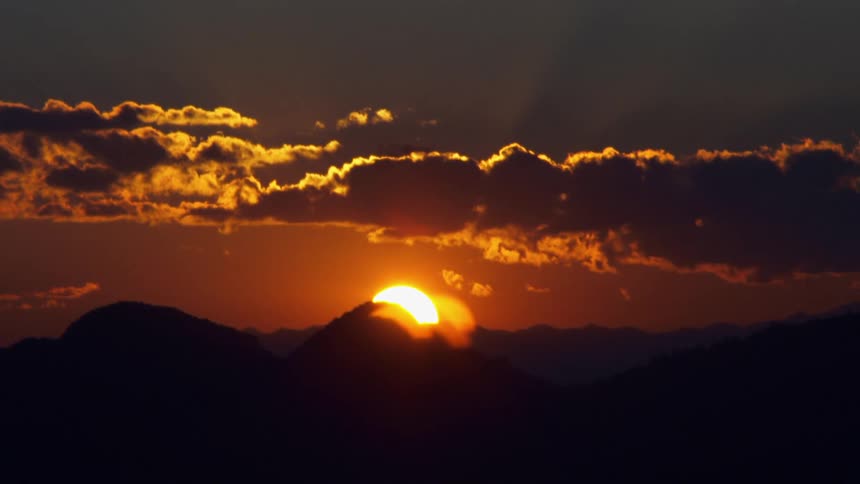 Sun turns sky orange as it sink behind mountain peak