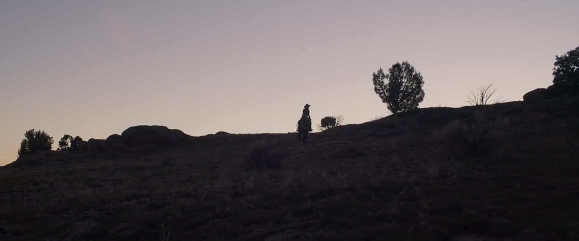 A silhouette of a cowboy riding across a field at dusk