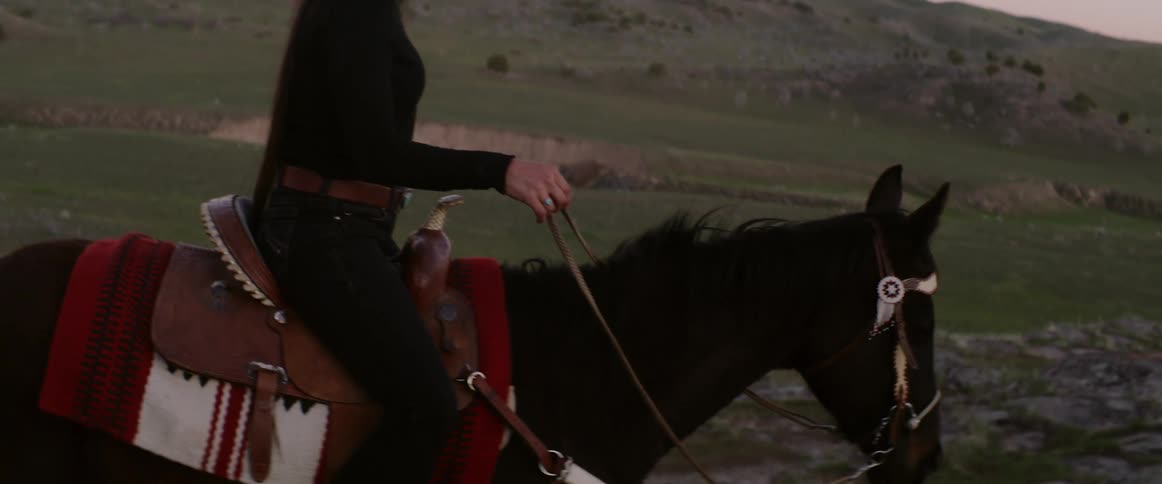 A woman rides horseback in a hilly rural area