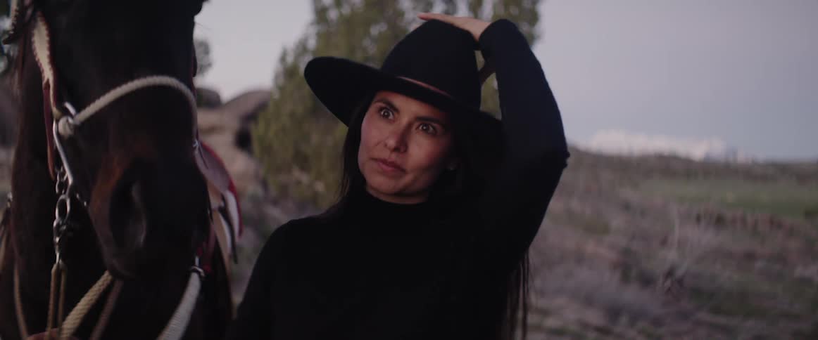 A woman holds on to her horse and puts a cowboy hat on