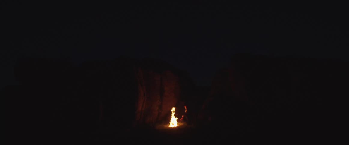Person sitting in front of a campfire between giant rocks in the desert at night