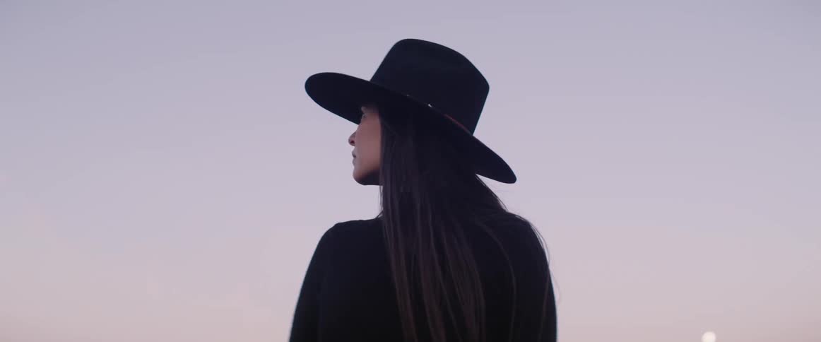 Woman with long hair wearing cowboy hat stands outdoors