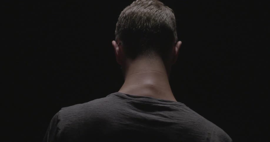 A man slowly moves his hands down from his head in a dark area